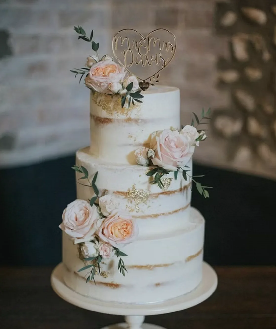 Three-tier white wedding cake with pink flowers and greenery