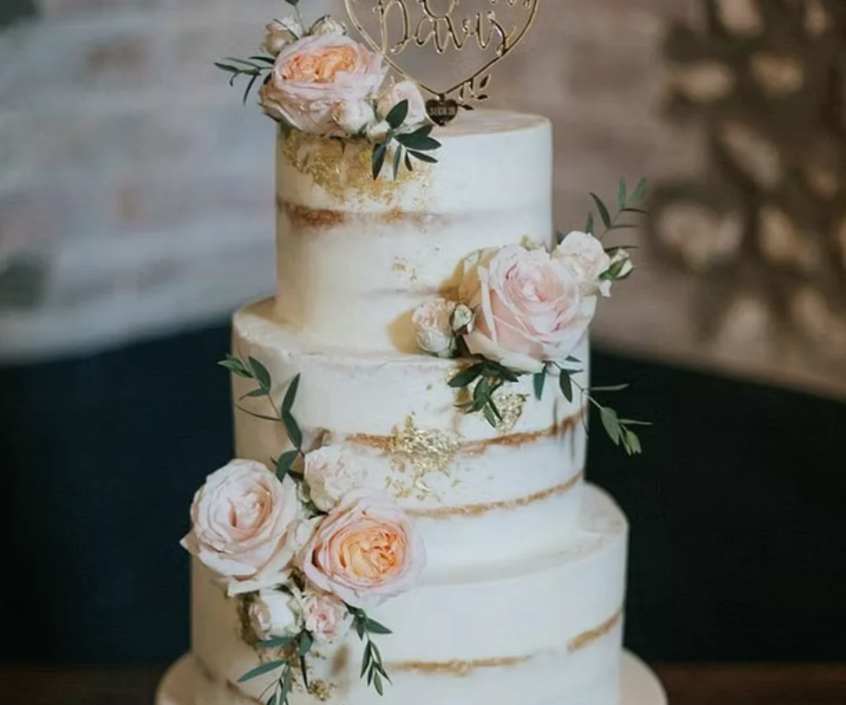 Elegant three-tier wedding cake with soft pink florals and greenery